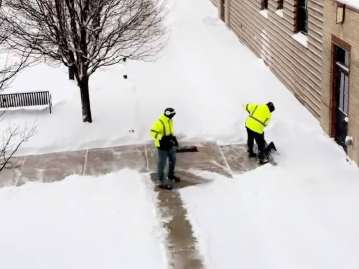 Two employees shoveling the sidewalks at a school
